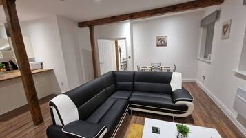 Un salon moderne avec un canapé d’angle noir, une table basse blanche et un tapis jaune.