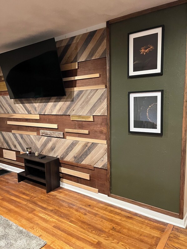 A modern living room with a herringbone wood wall, a flat-screen TV, and two framed pictures. - 12 min from Gainbridge, 10 min from Lucas Oil, 12 min from Motor Speedway (Indianapolis)