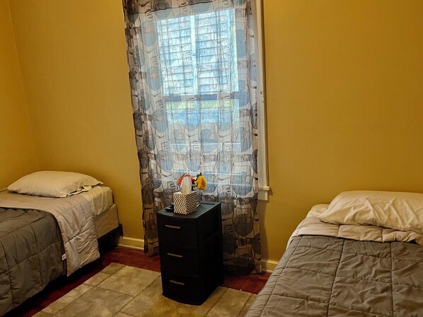 A bedroom with two beds, a nightstand, and a window with patterned curtains. - 12 min from Gainbridge, 10 min from Lucas Oil, 12 min from Motor Speedway (Indianapolis)