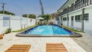 A swimming pool with a 6 ft 3 in depth, surrounded by a white fence, with a covered seating area and a staircase leading to a balcony.