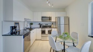 A modern kitchen with white cabinets, stainless steel appliances, a glass dining table, and a small potted plant.