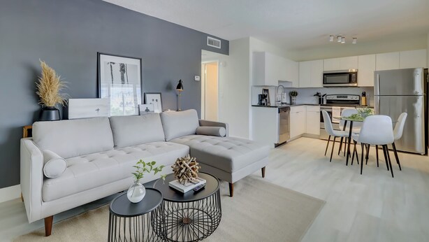 A modern living room with a grey sofa, a round coffee table, and a dining area with white chairs and a small table.
