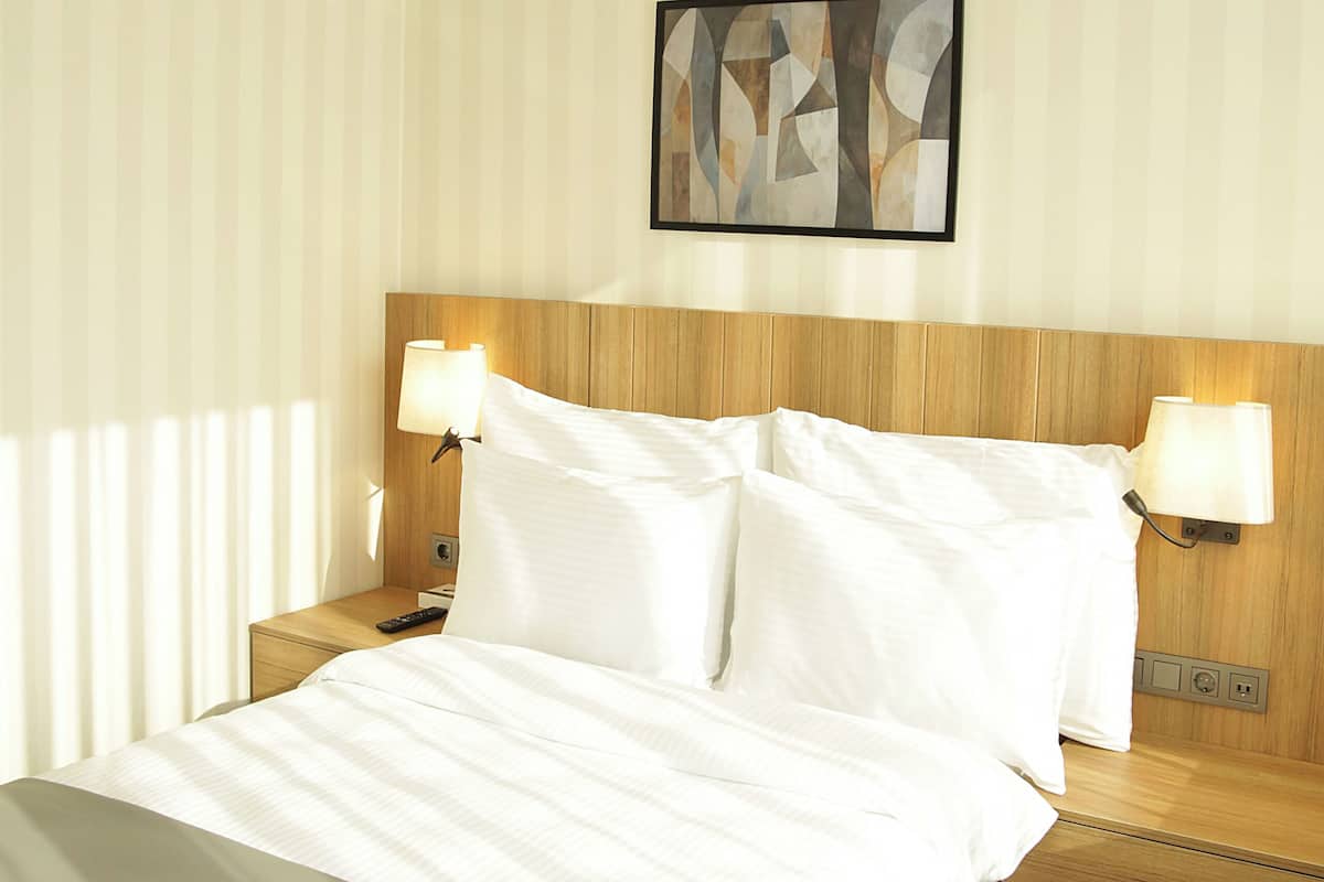 Una habitació d'hotel amb un llit, taules de nit i una obra d'art abstracta penjada a la paret.