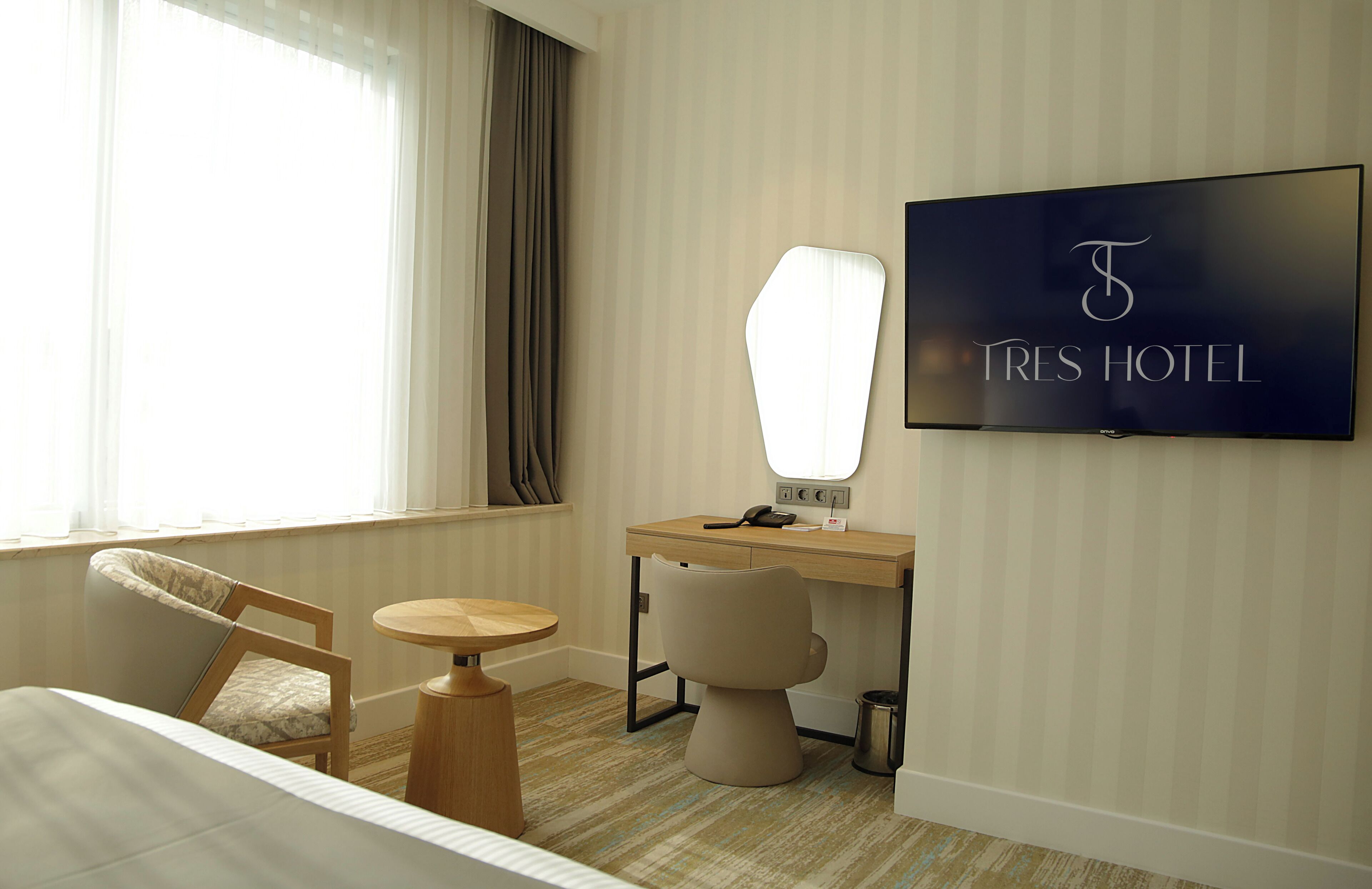 A hotel room with a bed, a desk, a chair, a round table, a TV, and a window with curtains.