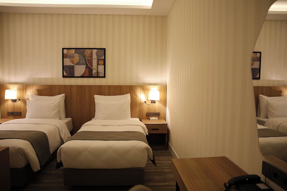 Habitació d'hotel amb dos llits, ambres de fusta, làmpades a cada costat del llit, un escriptori de fusta i un telèfon.