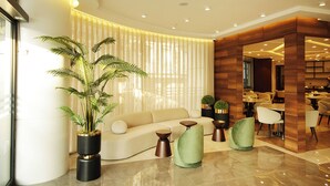A modern hotel lobby with a sofa, chairs, a large potted plant, and a dining area. - Tress Hotel (Istanbul)
