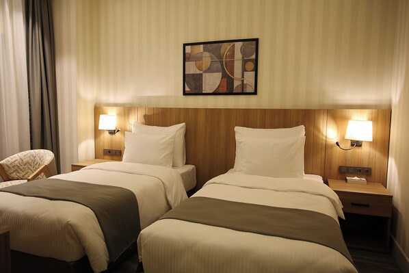 Habitación de hotel con dos camas, cada una con cabecera de madera, lámparas de noche y una paleta de colores neutros.