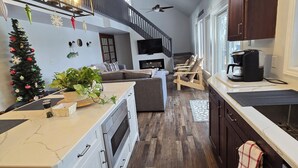 Uma cozinha moderna com ilha central, soalho de madeira e escada que dá para um andar superior.