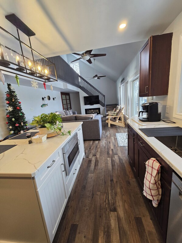 A modern kitchen with a central island, wooden flooring, and a staircase leading to an upper level.