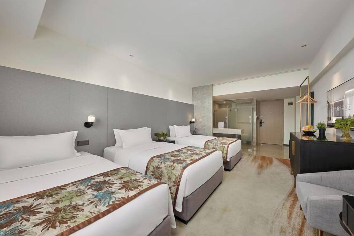 Une chambre d’hôtel avec trois lits, un canapé, un bureau et une salle de bain visible à travers une porte ouverte.