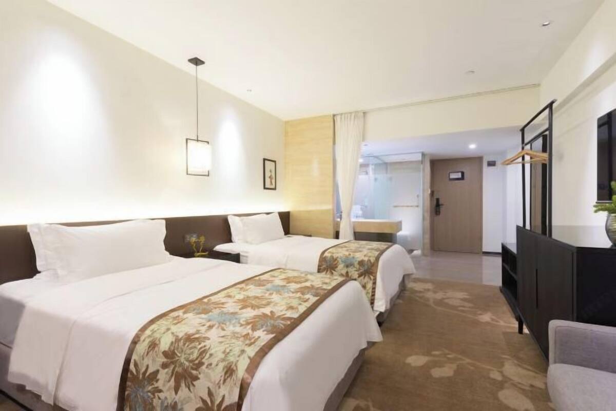 Une chambre d’hôtel avec deux lits, un téléviseur à écran plat, un bureau et une salle de bain visible à travers une porte.