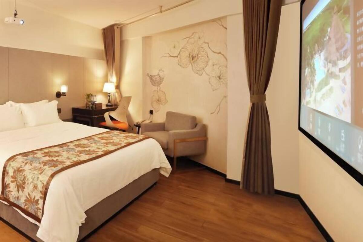 Une chambre d’hôtel avec un grand lit, un bureau, une chaise, une lampe et un téléviseur fixé au mur.