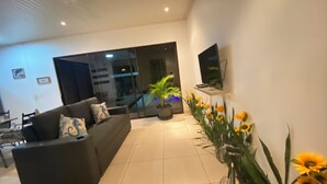 A modern living room with a sofa, a TV mounted on the wall, a potted plant, and a large window. - Lapas House (Garavito)