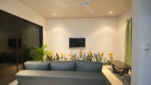 A modern living room with a grey sofa, a flat-screen TV mounted on the wall, and a ceiling fan. - Lapas House (Garavito)
