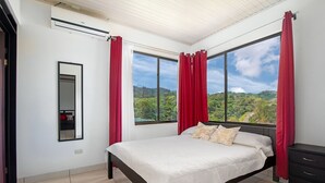 A bedroom with a large bed, a mirror, and a view of a green landscape through large windows. - Lapas House (Garavito)