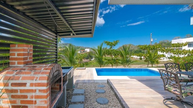 A modern outdoor patio with a brick oven, a pool, and a view of the surrounding landscape. - Lapas House (Garavito)