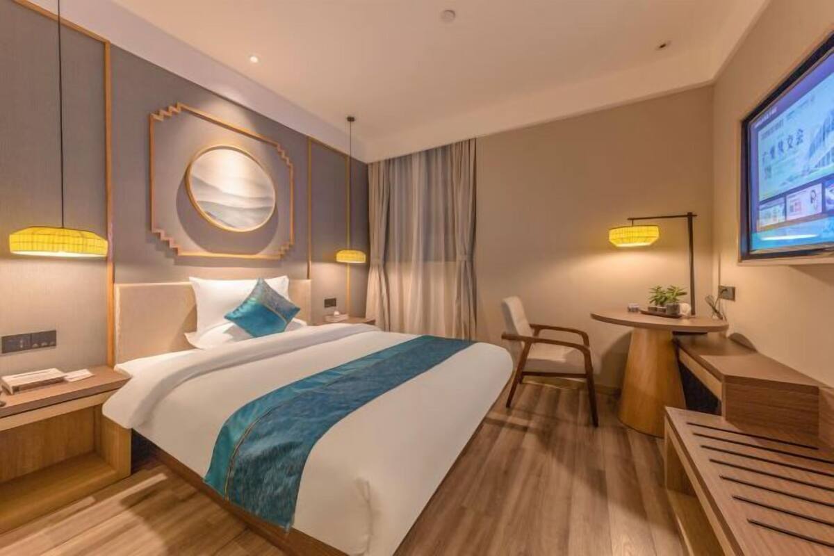 A modern hotel room with a large bed, a desk, and a TV screen.