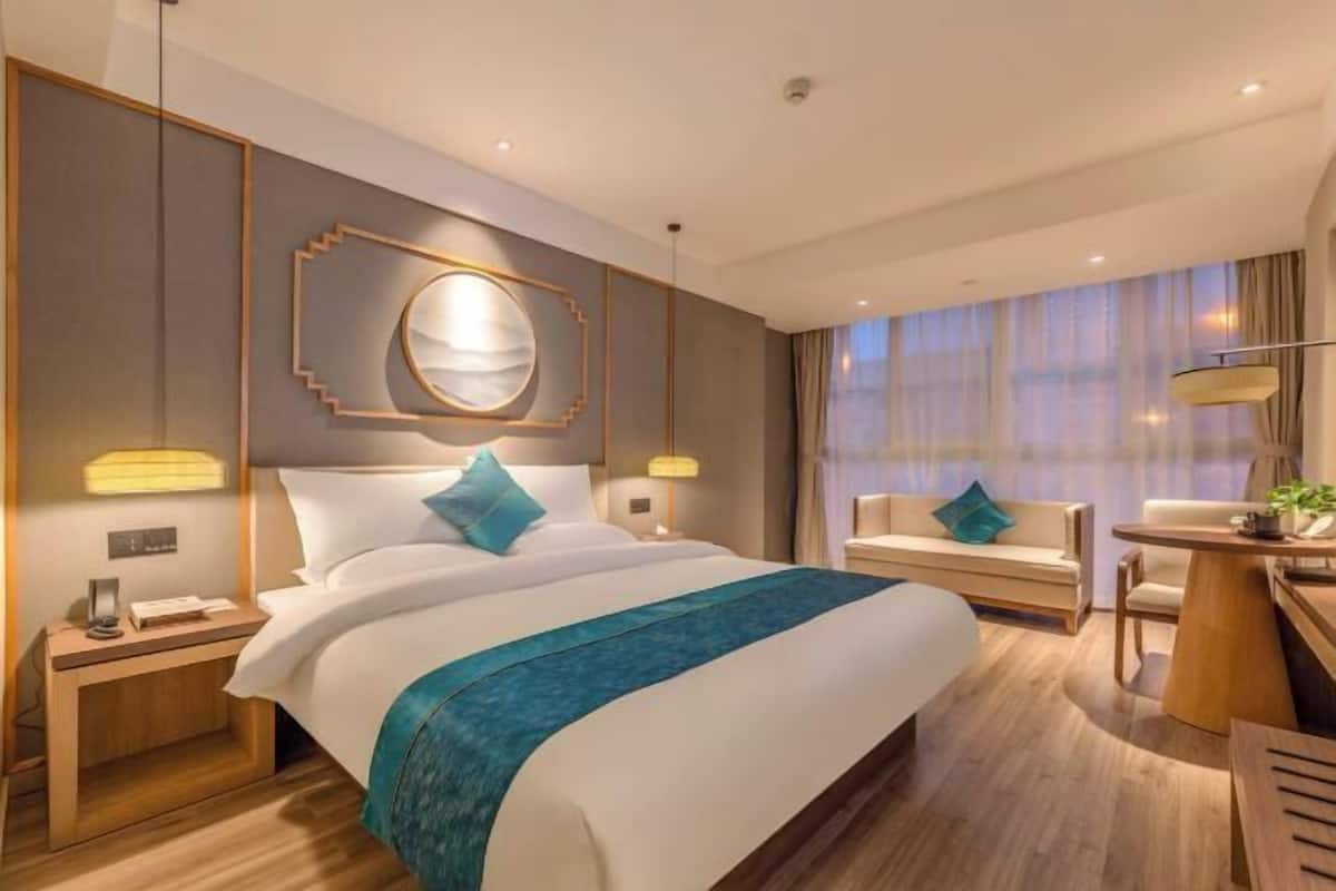 A modern hotel room with a large bed, a desk, and a sofa.