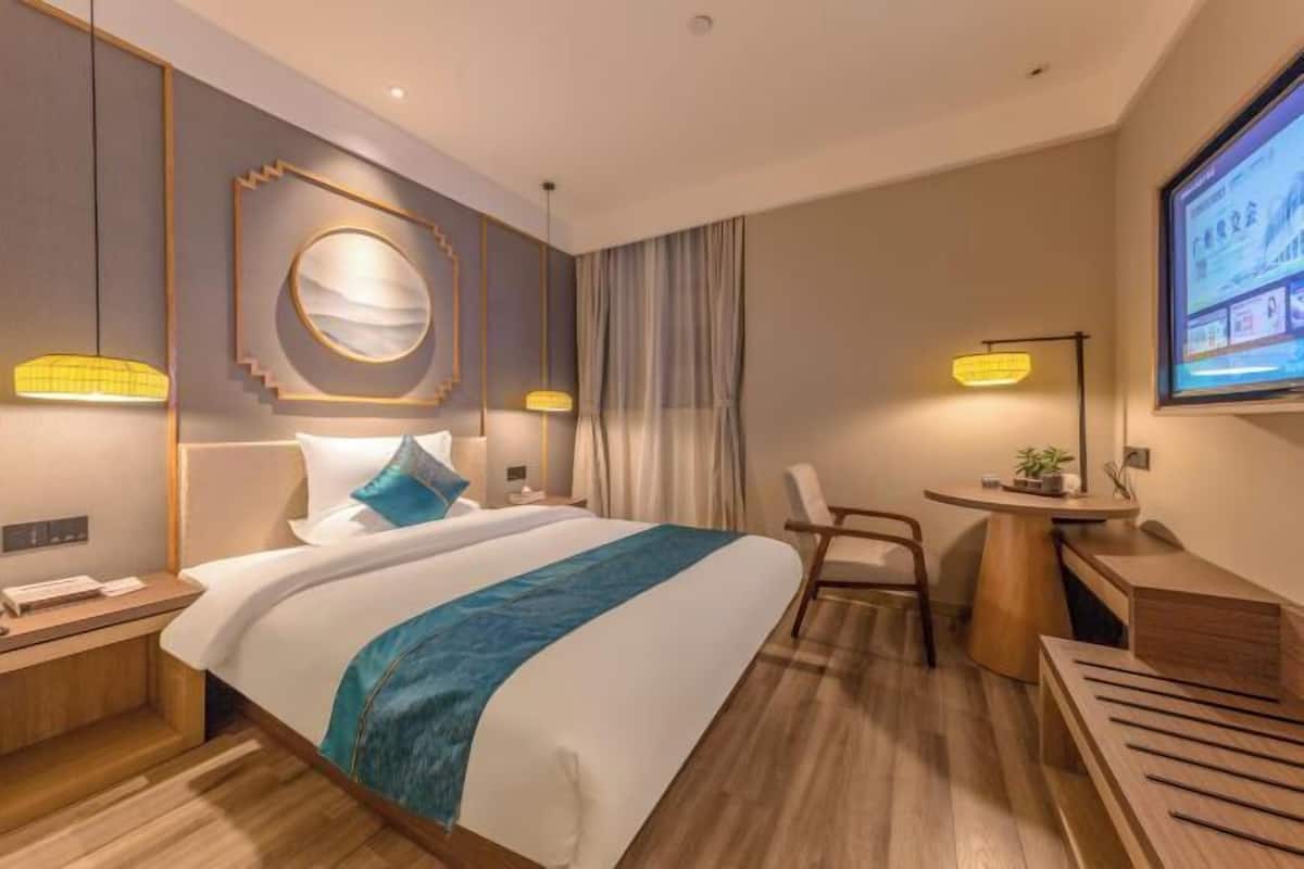 A modern hotel room with a large bed, a desk, and a TV screen.