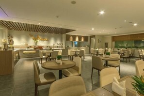 A modern hotel dining area with round tables, chairs, and a central kitchen area. - Fairyland Premium Hotel (Kunming Tuodong Sports Center Tangzixiang Metro Station) (Kunming)