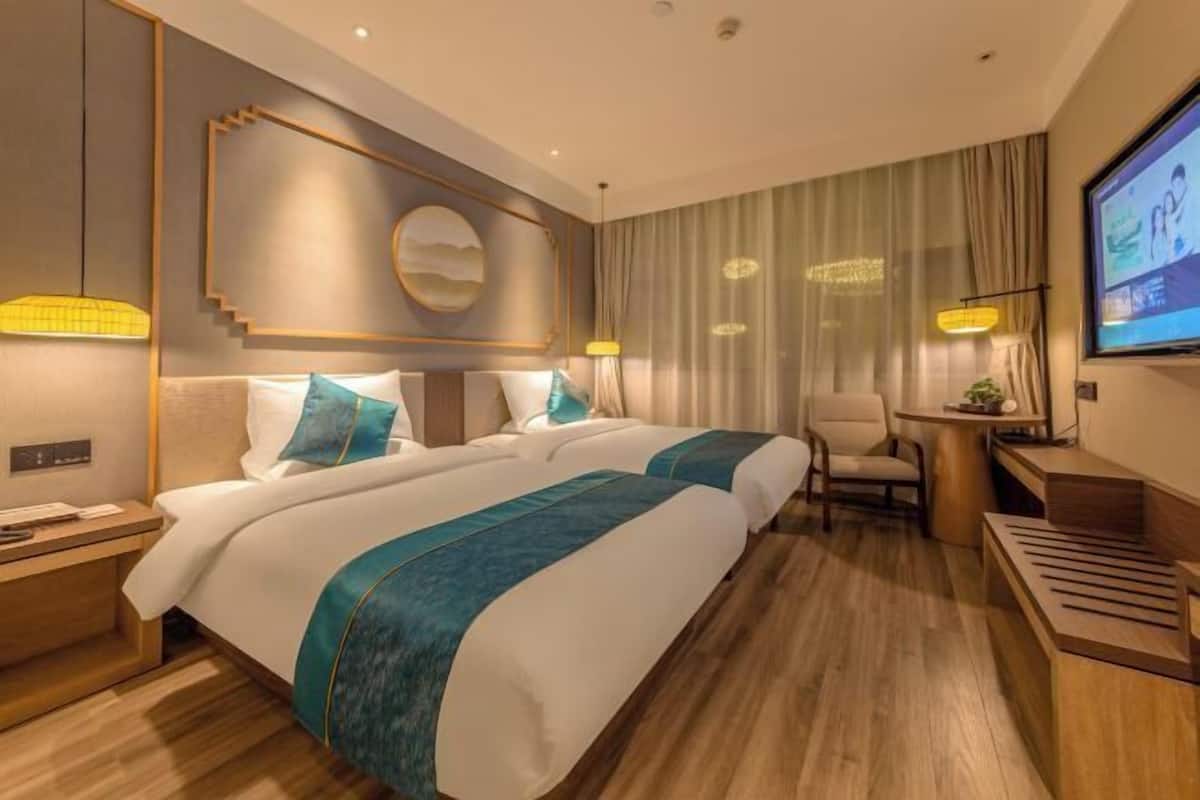 A hotel room with two beds, a desk, a chair, a TV, and a large window with curtains.