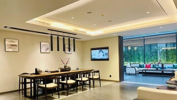 Uma sala de jantar moderna com uma mesa comprida e cadeiras, uma televisão na parede e um espaço de estar com sofás e uma mesa de centro.