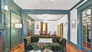 A room with a green velvet sofa, a round coffee table with a vase and book, and a chandelier.