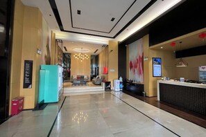 A modern hotel lobby with a reception desk, seating area, and a staircase leading to the upper floors.