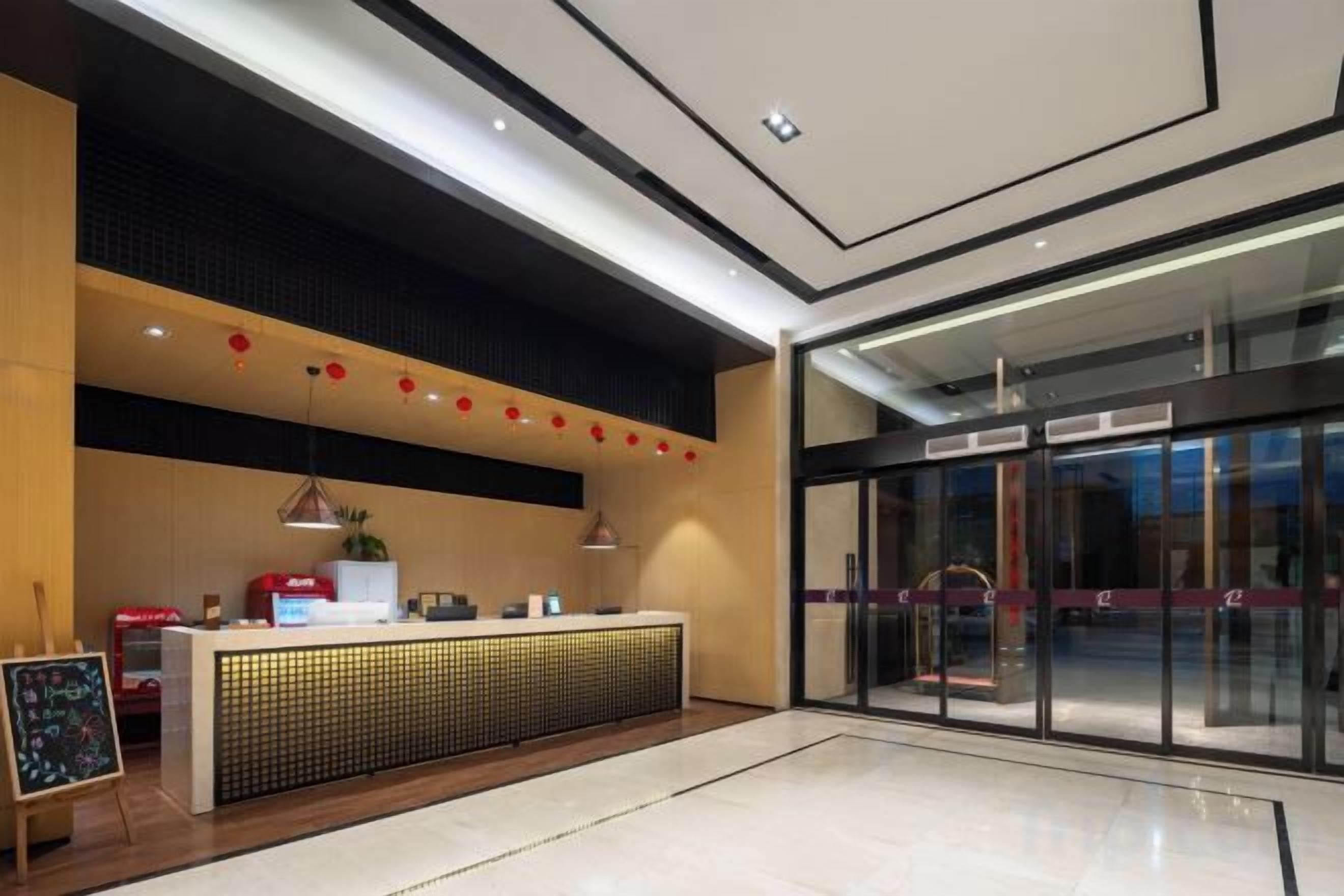 Ein Hotel-Empfangsbereich mit Empfangstresen, einer Tafel und einem Glastür-Eingang.