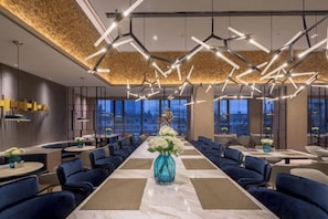 Un hall d’hôtel moderne avec une longue table à manger, des chaises rembourrées en tissu bleu et des luminaires contemporains.