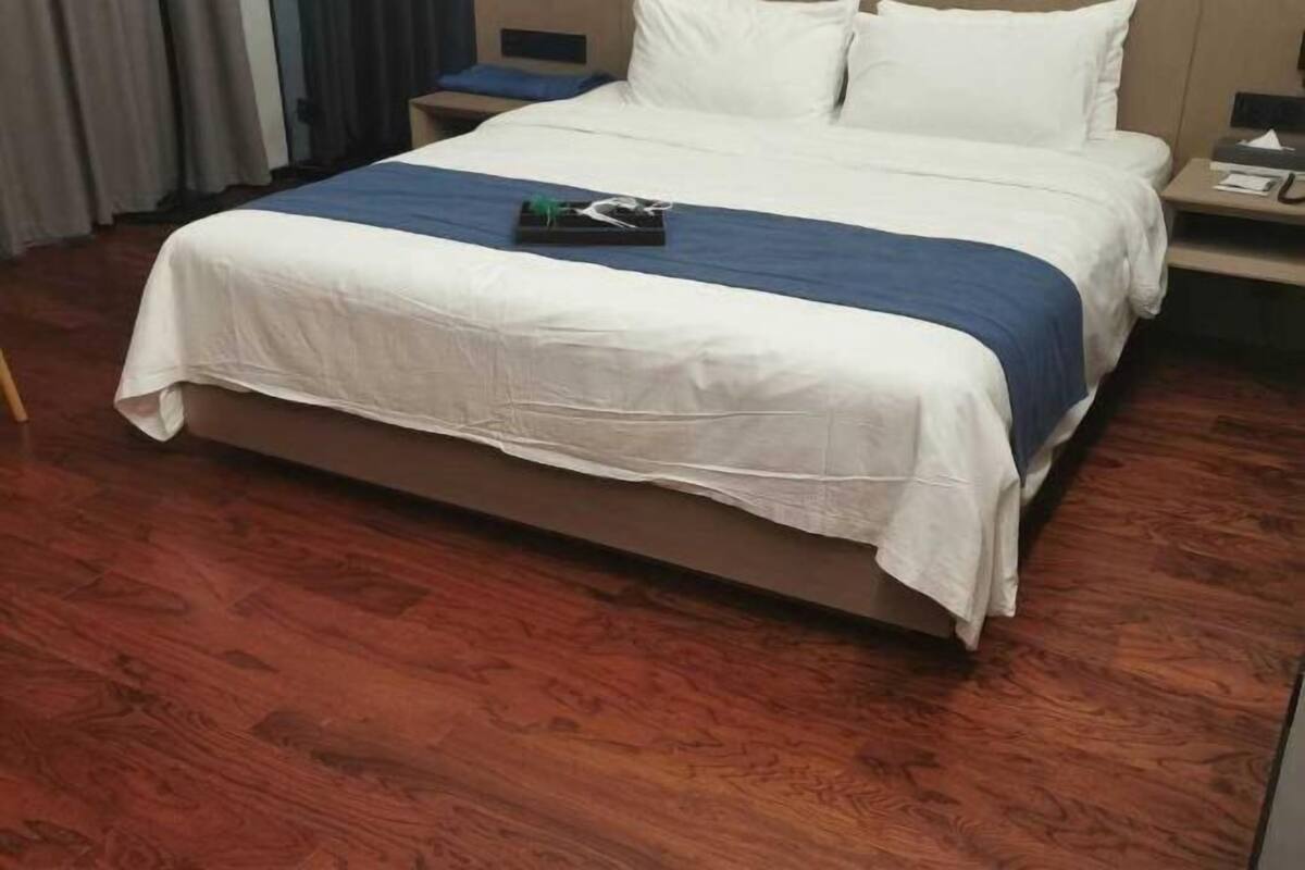 Un lit bien fait, recouvert d’une couvre-lit blanche et bleue, un plancher en bois et une table de chevet avec une lampe et une boîte de mouchoirs.
