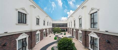 A courtyard with a central pathway, surrounded by white buildings with brick accents and arched windows.