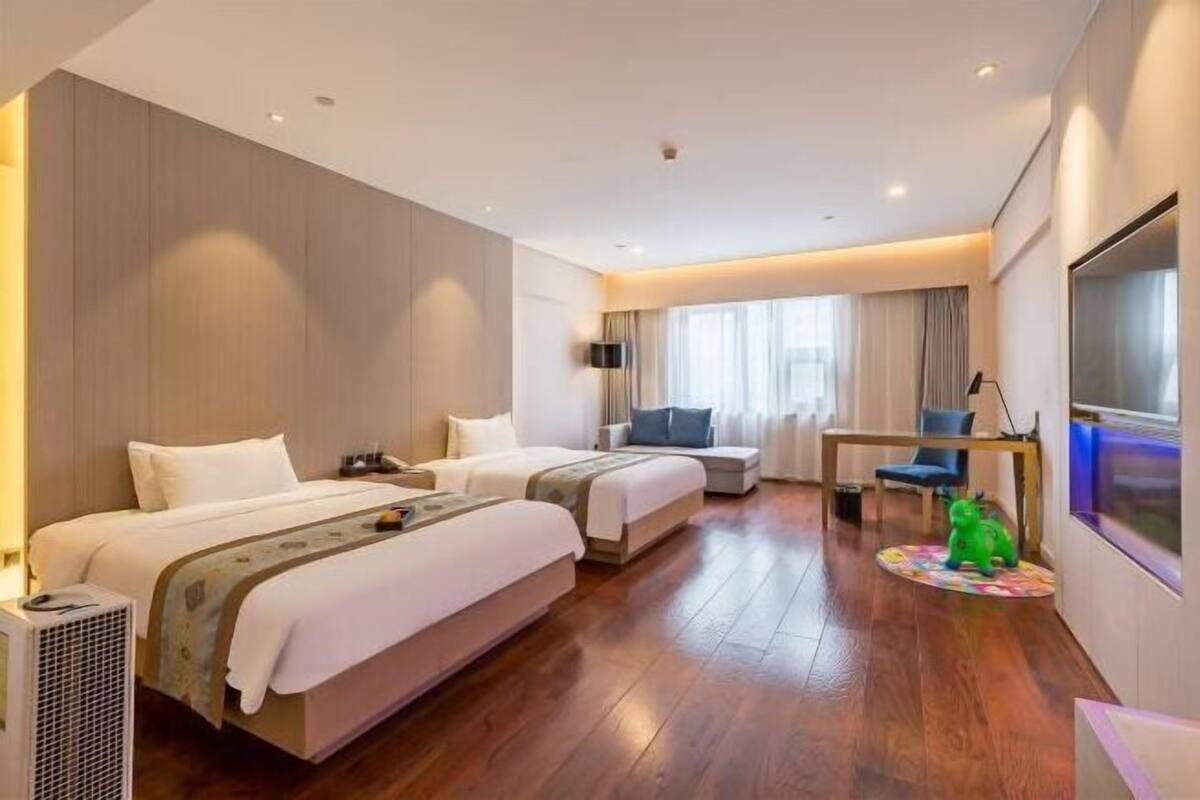 Une chambre d’hôtel avec deux lits, un bureau, une télévision et une fenêtre avec des rideaux.