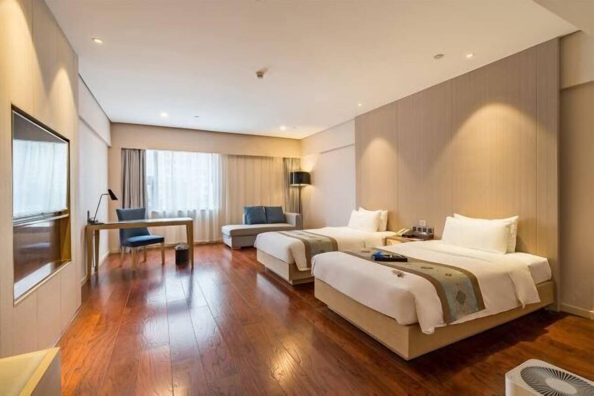 Une chambre d’hôtel avec deux lits, un bureau, une chaise et une grande fenêtre.