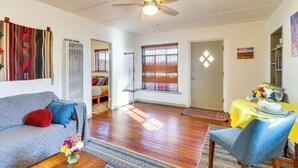 A spacious living room with a ceiling fan, a sofa, a dining table set for two, and a window with blinds.