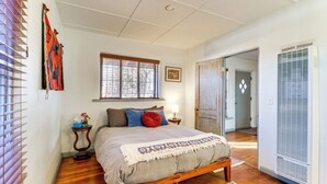 A bedroom with a wooden bed, a window with blinds, a bedside table with a lamp, and a rug on the floor.