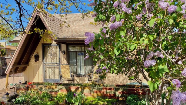 A house with a sloped roof, a front porch with chairs, and a garden with various plants and flowers.