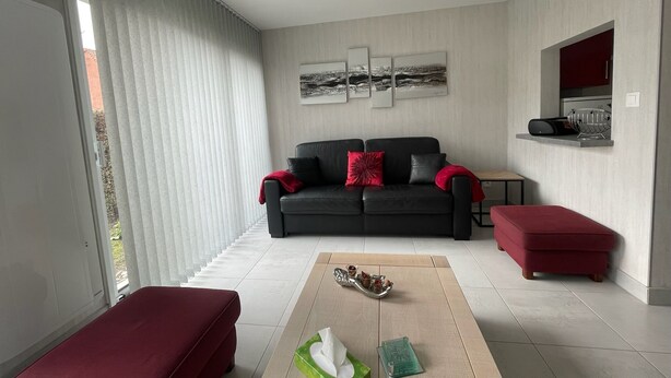 A modern living room with a black sofa, red cushions, a red ottoman, and a coffee table with a tissue box and decorative items. - Modern and Bright home walk to beach with garage (Berck-Plage)