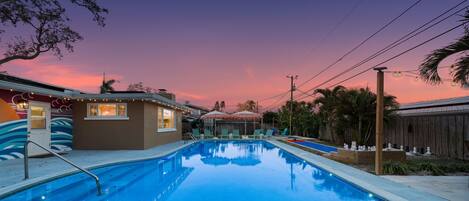 A swimming pool with lounge chairs and a wooden deck, surrounded by a wooden fence and palm trees.