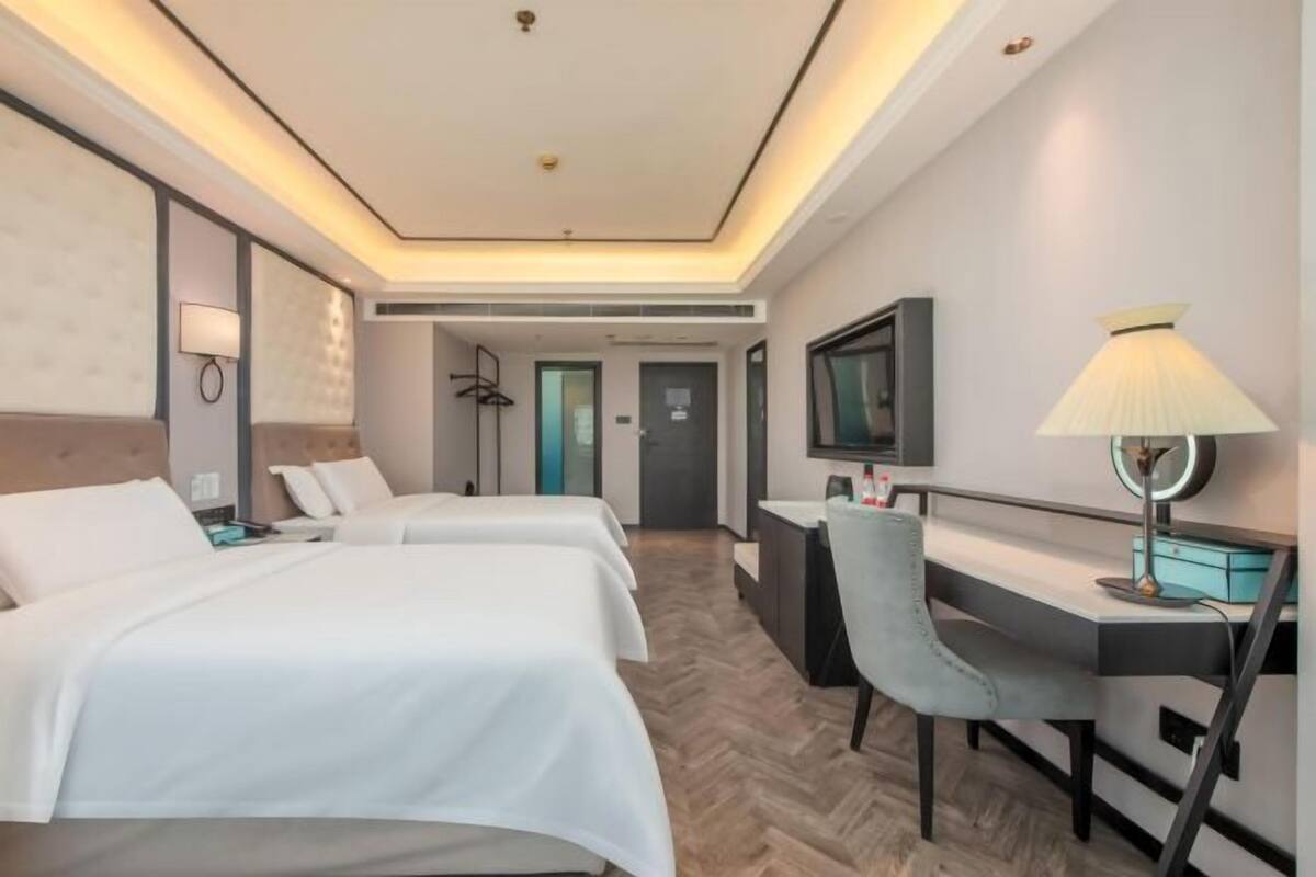 Una habitación de hotel con dos camas, un escritorio, una silla, un televisor y una lámpara.