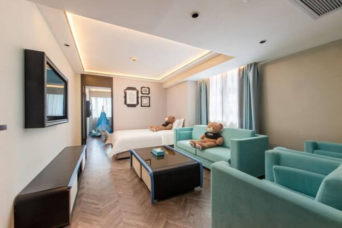 Una habitación de hotel moderna con cama, sofá, mesa de centro y televisor montado en la pared.