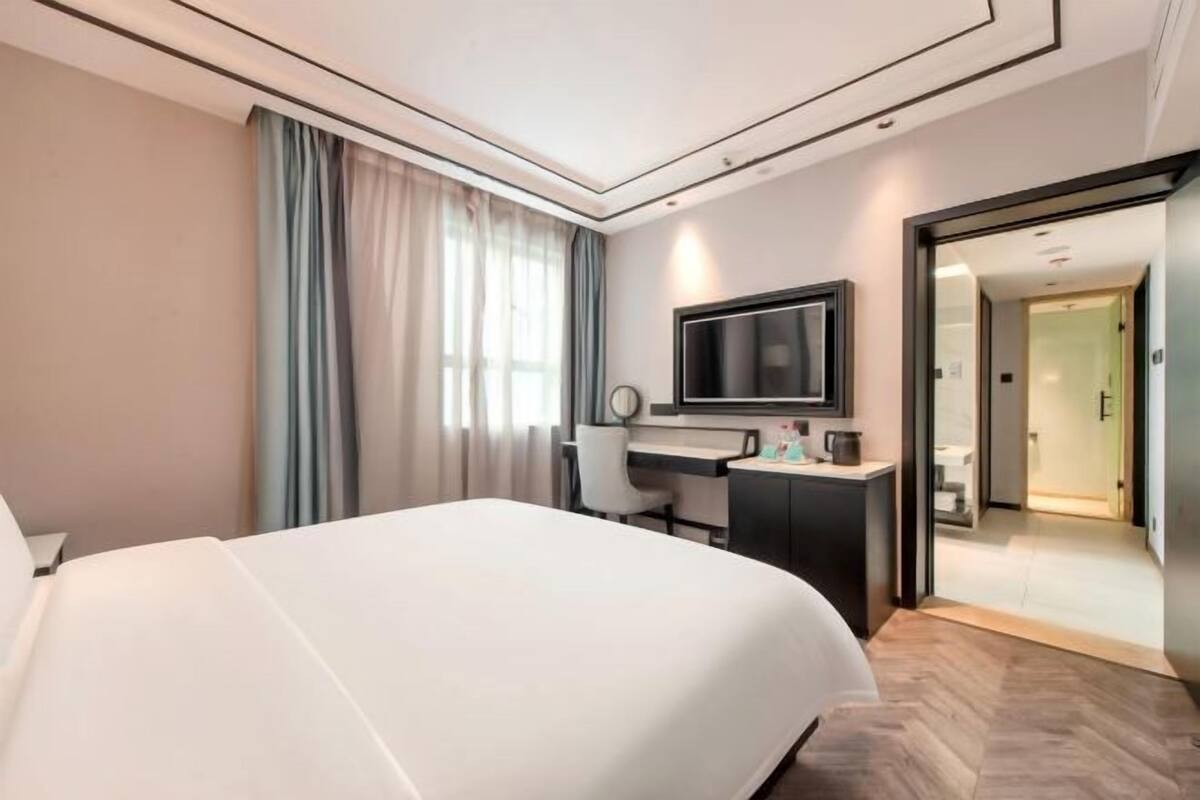 Habitación de hotel con una cama grande, un escritorio, un televisor y una puerta corredera que da a un baño.