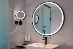 A modern bathroom with a large mirror, a round vanity mirror, and a white sink.