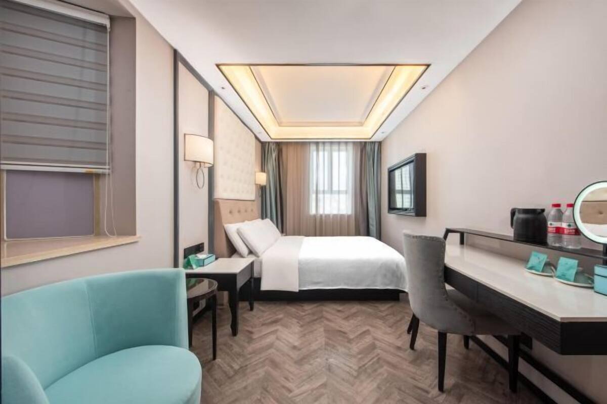 Habitación de hotel con cama, escritorio, silla y un ventanal con cortinas.