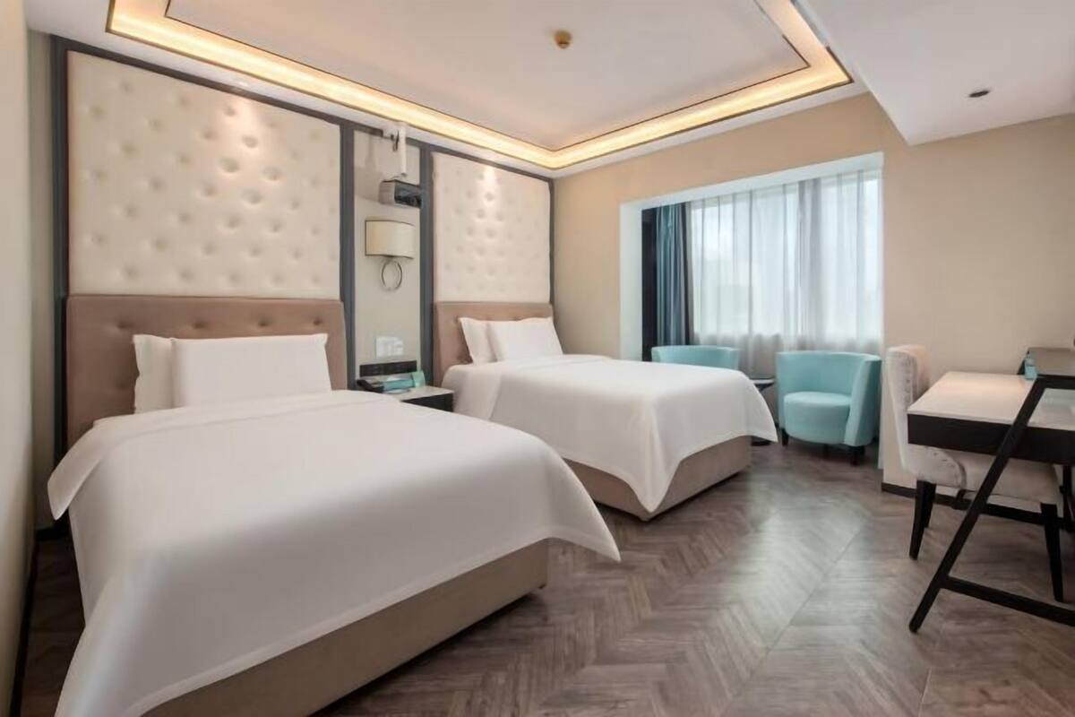 Habitación de hotel con dos camas, un escritorio, una silla, un ventanal con cortinas y un diseño moderno de techo.