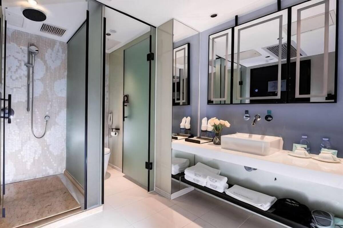 Un baño moderno con ducha acristalada, un espejo grande y tocador con lavabo y toallero.