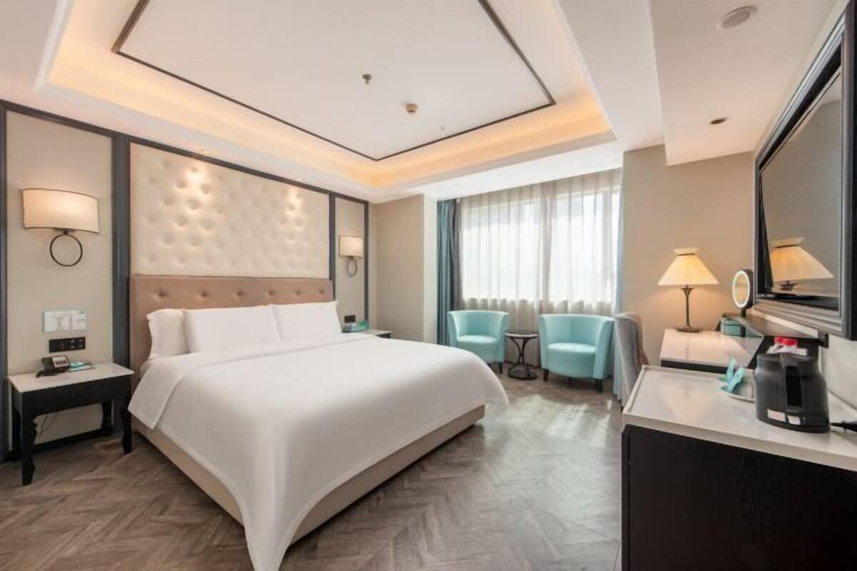 Habitación de hotel con una cama grande, un escritorio, dos sillones, una cafetera y un espejo.