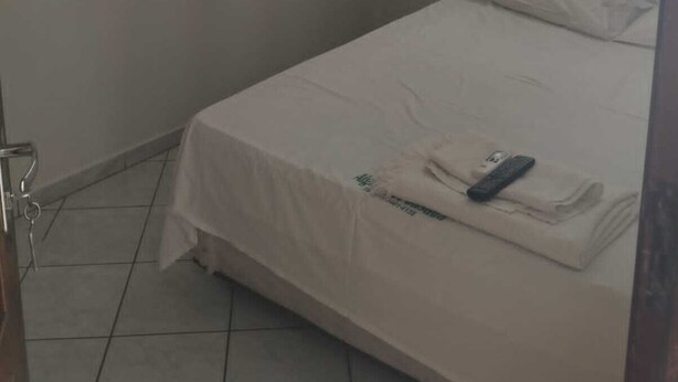Una stanza piccola e pulita con un letto singolo, un comodino e una finestra con tende leggere.