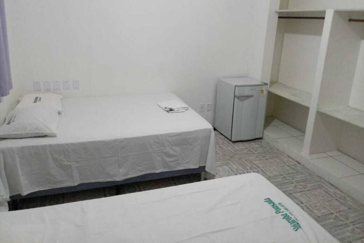 Une petite pièce propre, équipée d’un lit simple, d’un bureau et d’un réfrigérateur compact.