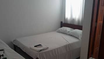 A small, simple room with two single beds, a small table, and a cabinet.